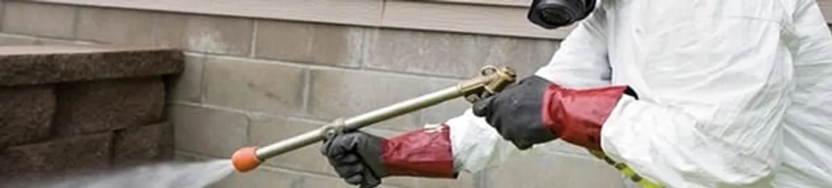 Pest control technician applying exterior insect treatment along a home foundation in Peoria, IL
