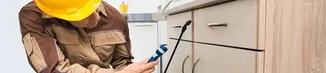 Roach exterminator applying treatment under kitchen cabinets in Peoria, IL
