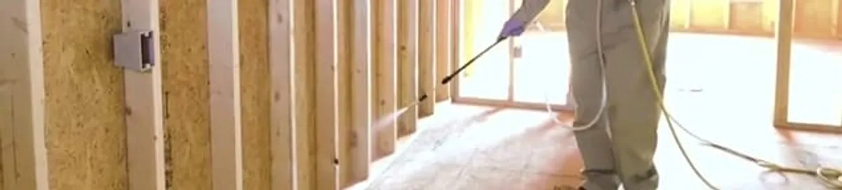 Termite treatment technician applying spray along framing and unfinished walls in Peoria, IL